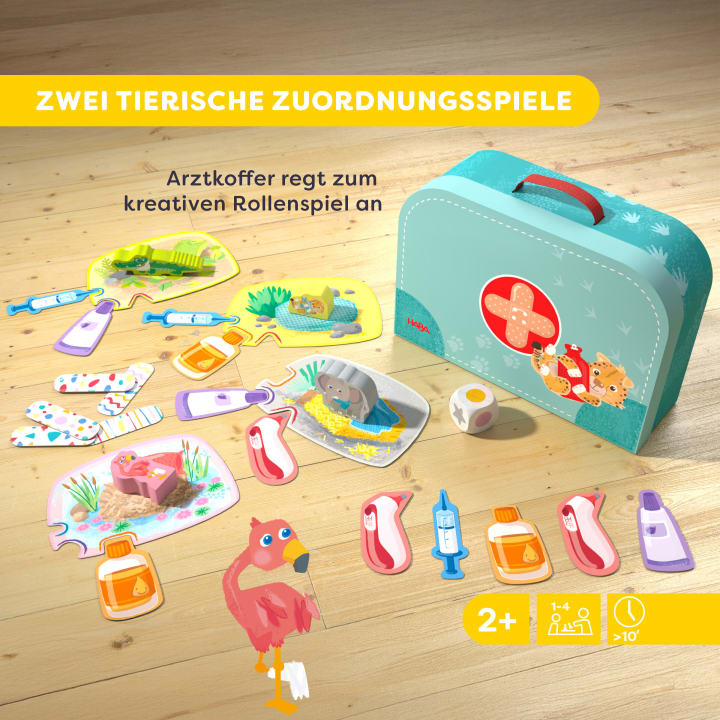 Auf einem Holzboden ist ein tierisches Kinderspiel ausgestellt, das aus Puzzleteilen mit Tieren, medizinischen Gegenständen und einem blauen, mit Tierbildern verzierten Spielzeug-Arztkoffer besteht. Der Text ist auf Deutsch.