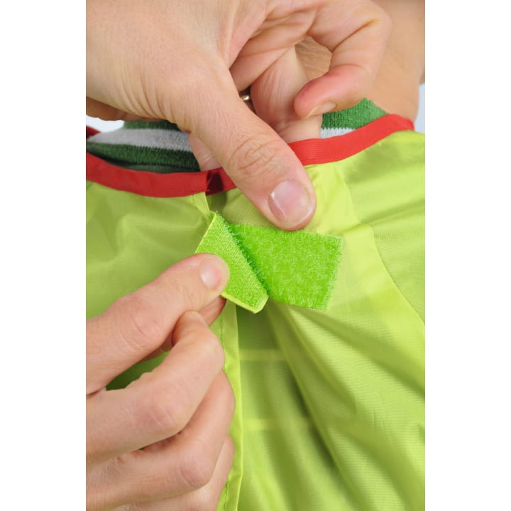 Nahaufnahme von Händen, die ein Stück grünes Klettband auf einem leuchtend grünen Stoff mit roter Umrandung befestigen.