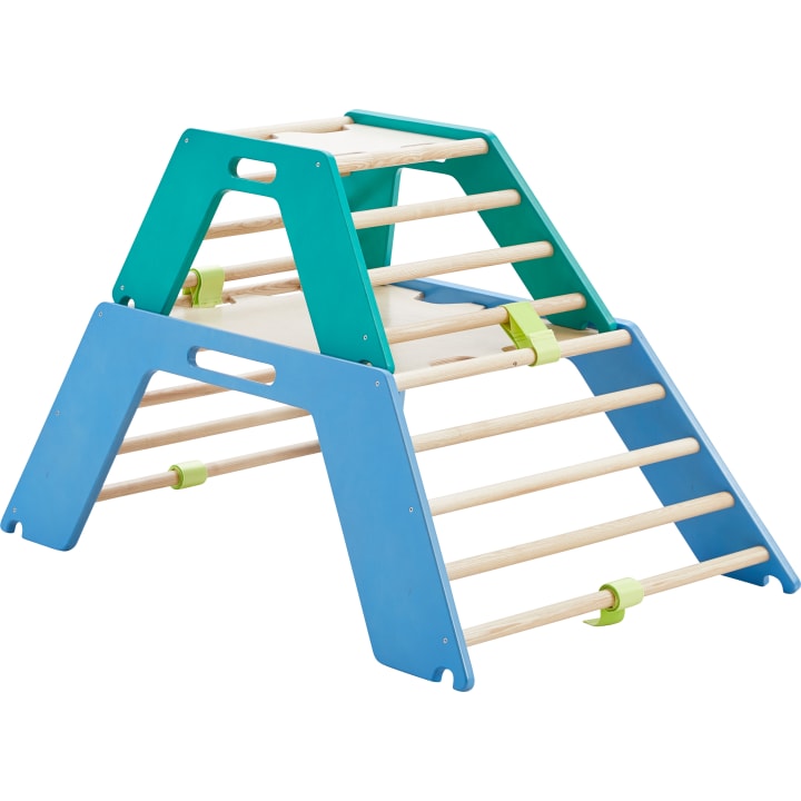 Ein hölzernes Kletterdreieck mit blauen und grünen Seitenwänden, Holzsprossen und grünen Verbindungselementen, das für das Spielen und die körperliche Betätigung von Kindern im Haus konzipiert wurde.