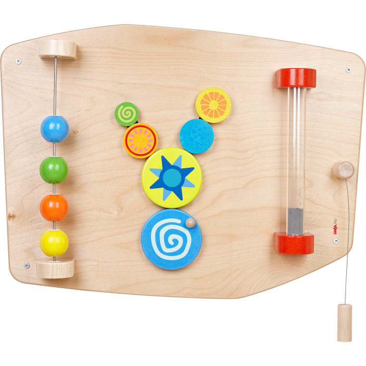 Ein Holzbrett für sensorische Aktivitäten mit bunten Perlen auf Stäben, sich drehenden Scheiben mit Spiral- und Sternmustern und einem vertikalen Rohr mit einem Knopf und einer Schnur auf der rechten Seite.