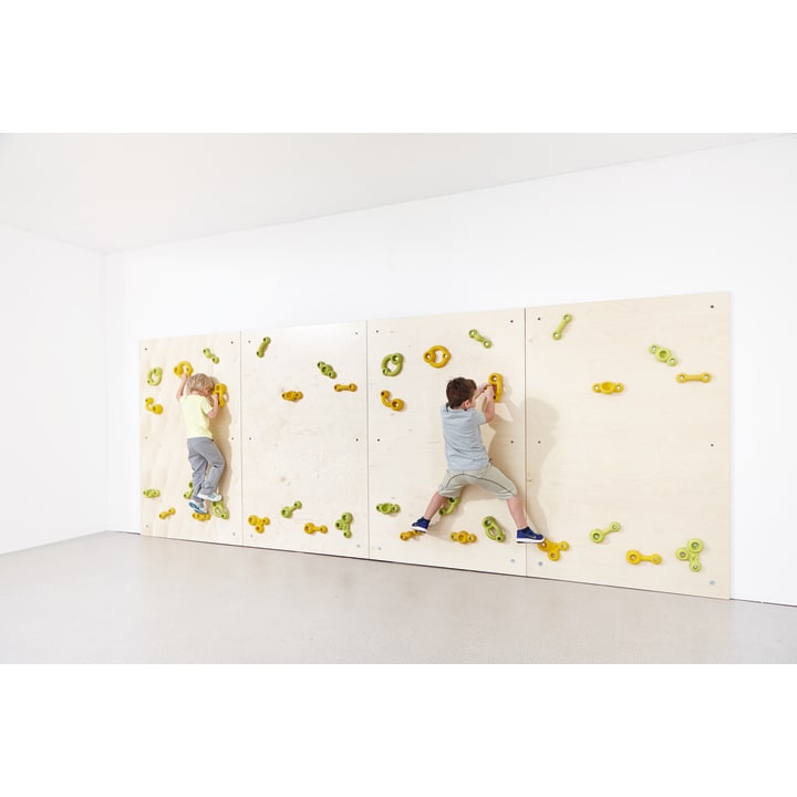 Zwei Kinder klettern an einer hellen Indoor-Kletterwand mit grünen und gelben Griffen, die sich von einer schlichten weißen Wand und einem weißen Boden abhebt.