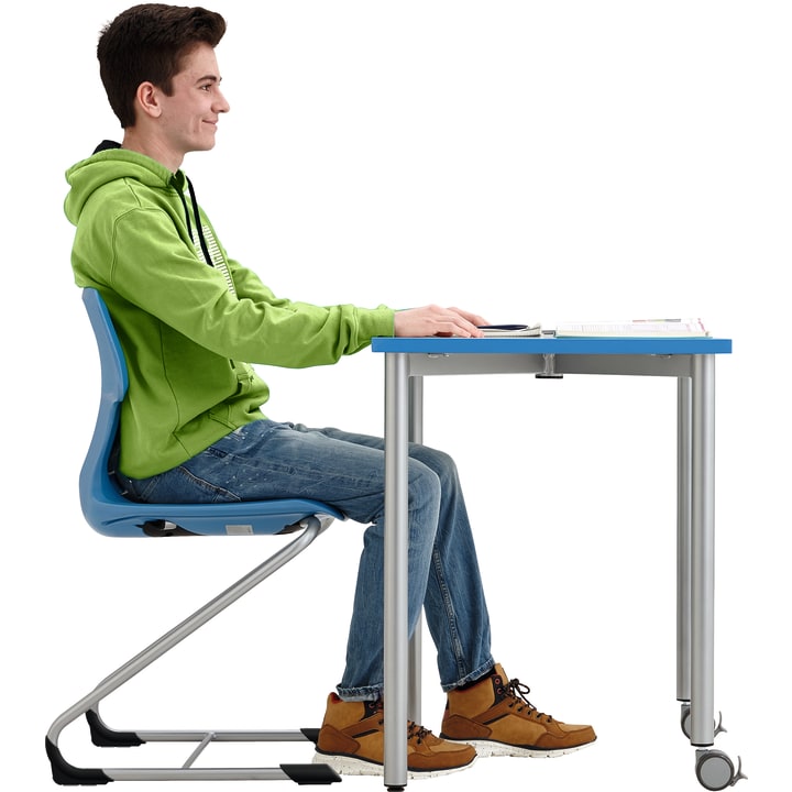 Eine junge Person in grünem Kapuzenpulli und Jeans sitzt aufrecht an einem blauen Schreibtisch, den Blick nach vorne gerichtet und die Hände auf den Tisch gestützt. Vor ihr liegt ein aufgeschlagenes Notizbuch. Der Hintergrund ist einfarbig weiß.