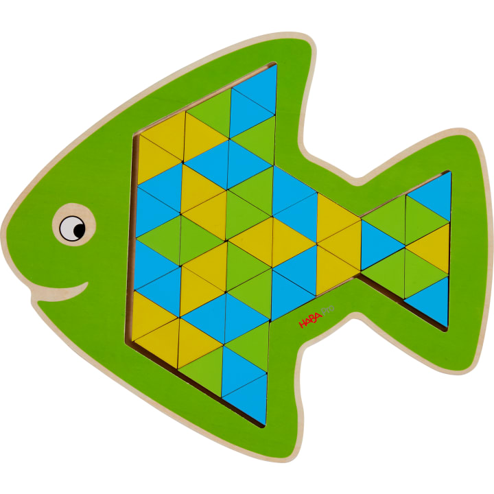 Ein grünes fischförmiges Holzpuzzle mit einem umrandeten Bereich, der mit kleinen blauen, gelben und grünen dreieckigen Teilen gefüllt ist, die in einem geometrischen Muster angeordnet sind. Der Fisch hat ein einfaches Auge im Cartoon-Stil und einen lächelnden Mund.