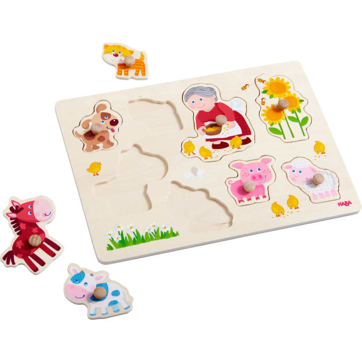 Ein Holzpuzzle mit Cartoon-Teilen von einem Pferd, einer Kuh, einem Hund, einer Katze, einem Schwein, Küken, Sonnenblumen und einer älteren Frau mit Honig. Einige Teile werden herausgenommen und neben das Brett gelegt. Jedes Teil hat einen Holzknauf zum Greifen.