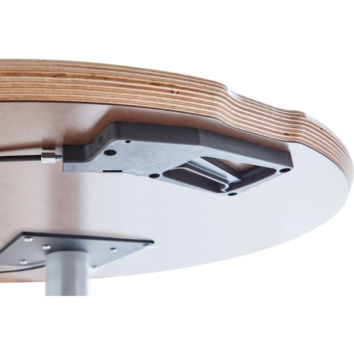 Nahaufnahme der Unterseite einer runden Holztischplatte, die einen schwarzen Mechanismus, der an der Oberfläche befestigt ist, und eine Stützstange aus Metall zeigt. Die geschichtete Kante des Holzes ist sichtbar.