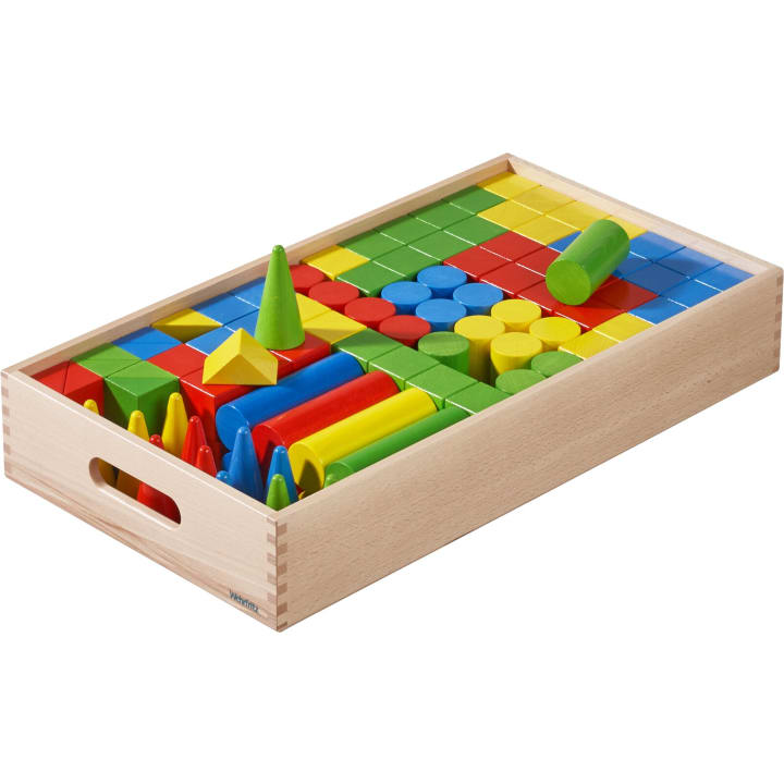 Ein Holztablett, gefüllt mit verschiedenen bunten Holzklötzen in unterschiedlichen Formen, darunter Würfel, Zylinder, Kegel und Prismen, die im Inneren des Tabletts ordentlich angeordnet sind.