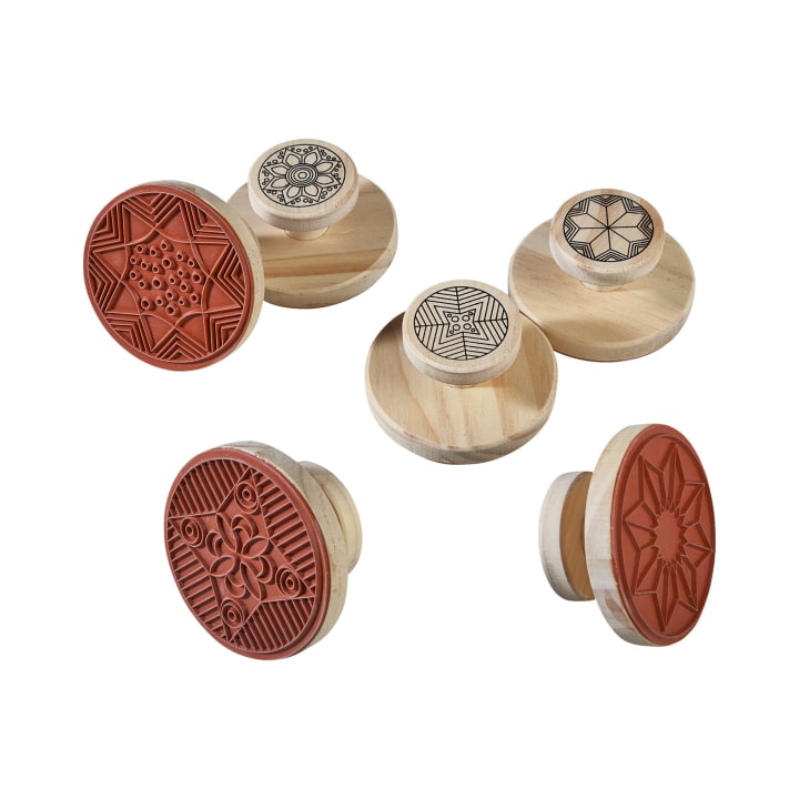 Fünf runde Holzstempel sind mit komplizierten geometrischen und floralen Mustern in die roten Gummistempeloberflächen eingeritzt; die Oberseiten der Stempel zeigen die gleichen Muster in Schwarz auf Holz.