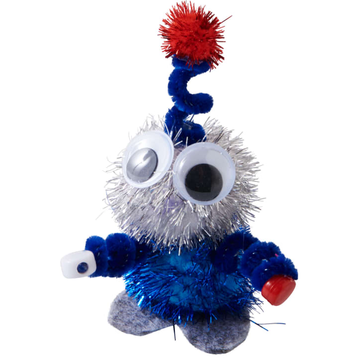 Eine kleine Bastelfigur aus blauem und silbernem Lametta, mit großen Kulleraugen, Pfeifenreinigerarmen, einem roten Bommel an der Spitze und Filzfüßen, die in jeder Hand kleine Plastikgegenstände hält.