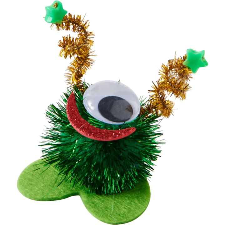 Eine grüne Bastelkreatur aus Lametta, mit einem großen Glupschauge, einem roten Glitzerlächeln, zwei goldenen Pfeifenreiniger-Antennen, die mit grünen Sternen besetzt sind, und grünen Filzfüßen.