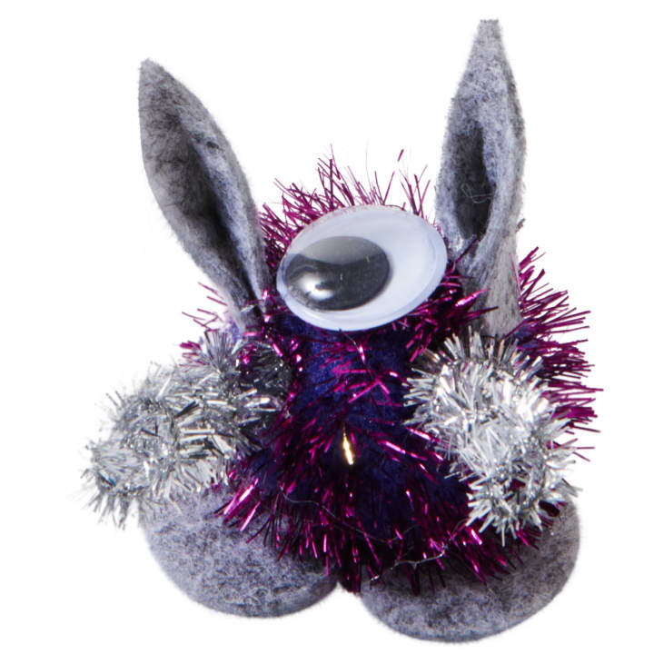 Eine kleine Bastelfigur aus lilafarbenem und silbernem Lametta, grauem Filz, zwei aufrechten Filzohren und einem einzigen großen Plastik-Googly-Auge auf der Spitze.