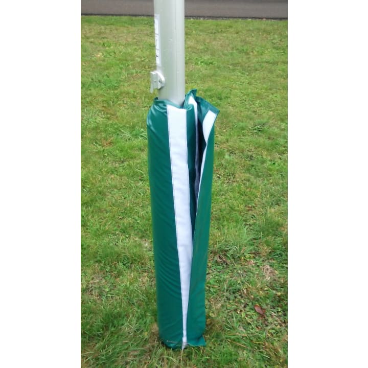 Eine grün-weiß gepolsterte Abdeckung ist um den Sockel eines Metallpfostens gewickelt, der auf einer Grasfläche in der Nähe einer gepflasterten Fläche steht. Die Abdeckung ist an einer Seite teilweise offen.
