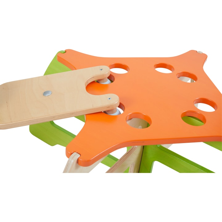 Nahaufnahme einer Holzkonstruktion mit einer orangefarbenen, sternförmigen Spitze mit kreisförmigen Löchern, die an grünen Stützen befestigt ist, und einem flachen Stück aus hellem Holz, das mit einem Metallbolzen verbunden ist.