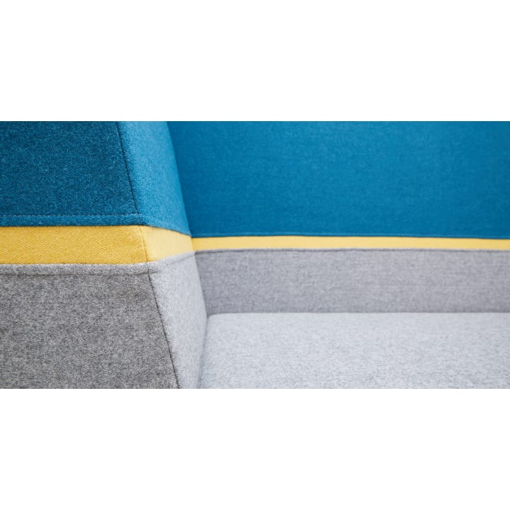 Nahaufnahme eines Polstermöbels mit blauen, gelben und grauen Stoffteilen. Das Bild zeigt die Ecke, an der Rückenlehne und Sitz aufeinandertreffen, und hebt die Textur und die klaren Linien des Materials hervor.