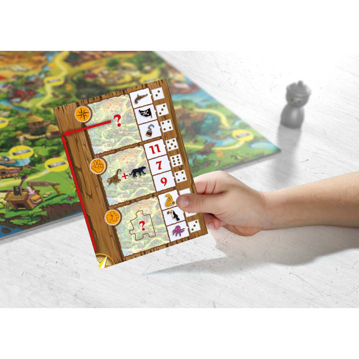 Eine Hand hält eine Spielkarte mit Tiersymbolen, Zahlen, Fragezeichen und Würfelbildern. Ein buntes Spielbrett und eine Figur sind im Hintergrund auf einer weißen Fläche zu sehen.