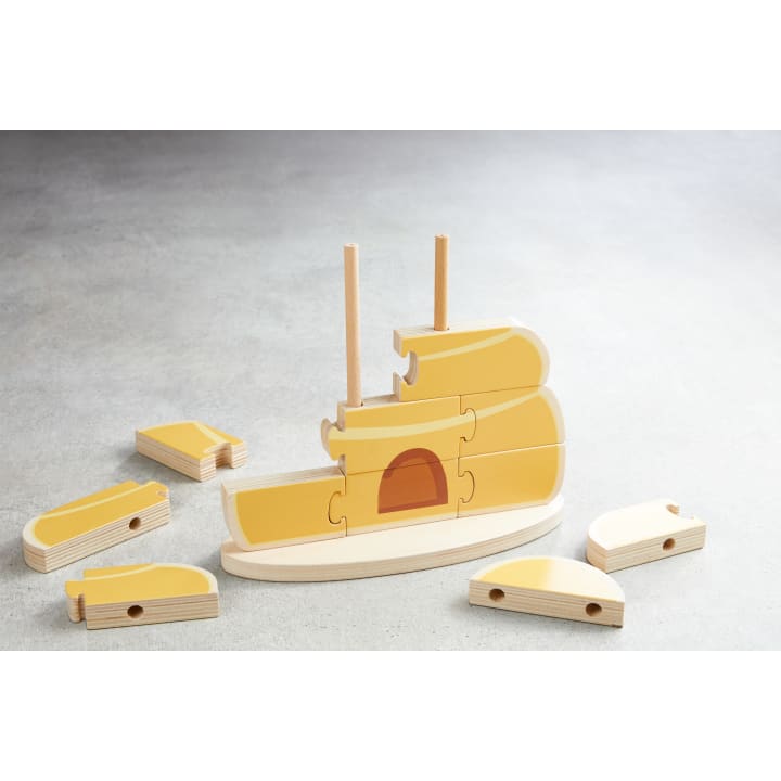 Ein Holzpuzzle in Form eines Schiffes mit mehreren gelben und naturfarbenen Holzteilen, von denen einige auf einem Holzsockel mit zwei vertikalen Stangen montiert sind, während andere Teile auf einer grauen Fläche verstreut liegen.