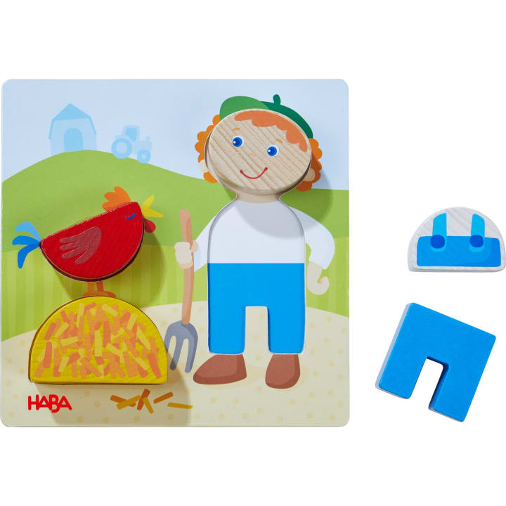 Ein Holzpuzzle zeigt einen Bauern, ein rotes Huhn, einen Heuhaufen und eine Mistgabel vor einem Bauernhofhintergrund. Zwei Puzzleteile - ein blauer Overall und ein blauer U-förmiger Block - befinden sich auf der rechten Seite des Puzzles.