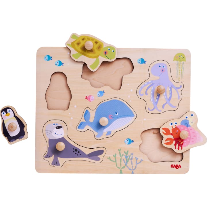 Ein Tierpuzzle aus Holz mit geformten Teilen, die eine Schildkröte, einen Pinguin, einen Wal, eine Robbe, einen Oktopus, eine Krabbe und einen Fisch darstellen. Einige Teile werden entfernt und außerhalb ihrer jeweiligen Schlitze platziert.