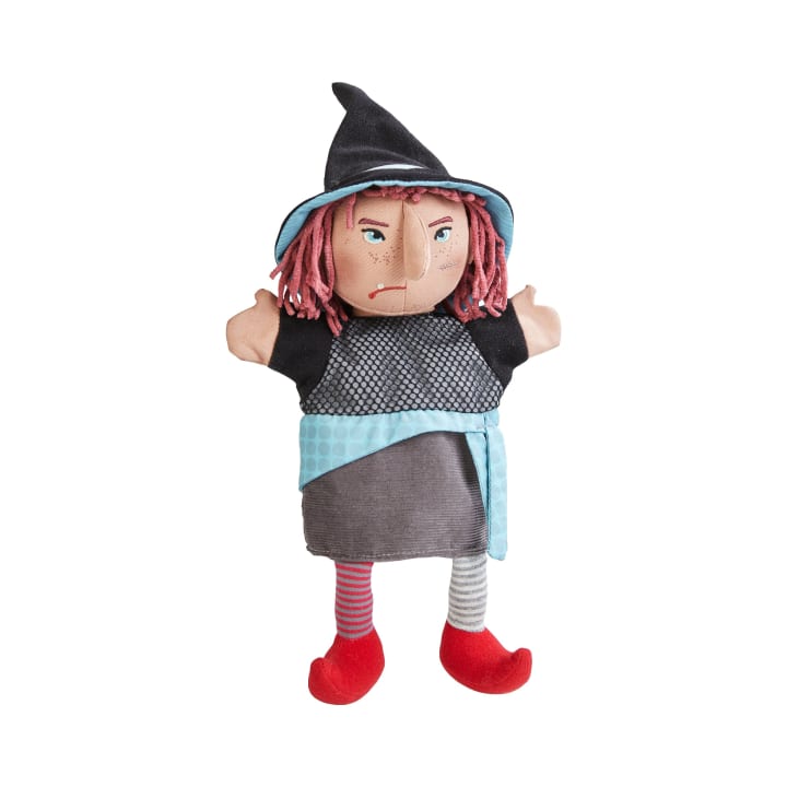 Eine Stoffhandpuppe einer Hexe mit einem spitzen schwarzen Hut, rotem Garnhaar, gestreiften Strümpfen, roten Schuhen und einem grauen Kleid mit blauer Schärpe, dargestellt vor einem weißen Hintergrund.