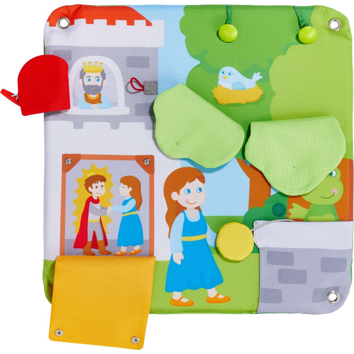 Ein farbenfrohes Aktivitätspaneel aus Stoff mit Cartoon-Illustrationen einer Prinzessin, eines Königs, eines Vogels in einem Nest und eines Froschs. Die Platte hat Klappen, Knöpfe und Texturen für interaktives Spiel.