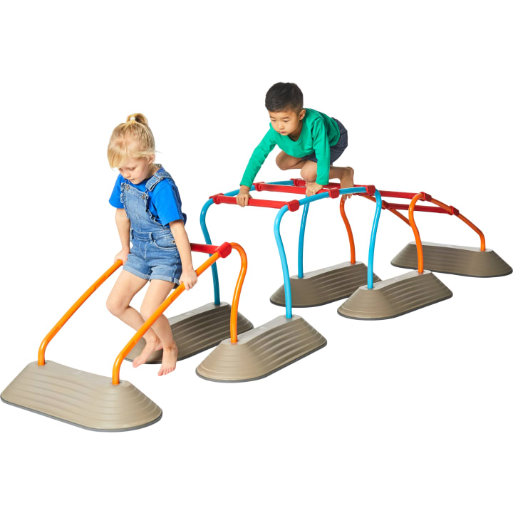 Zwei kleine Kinder, ein Mädchen und ein Junge, spielen auf einer Reihe von bunten Kletterstangen mit grauen Sockeln. Das Mädchen klettert von einem orangefarbenen Barren herunter, während der Junge über einen roten Barren klettert. Der Hintergrund ist weiß.