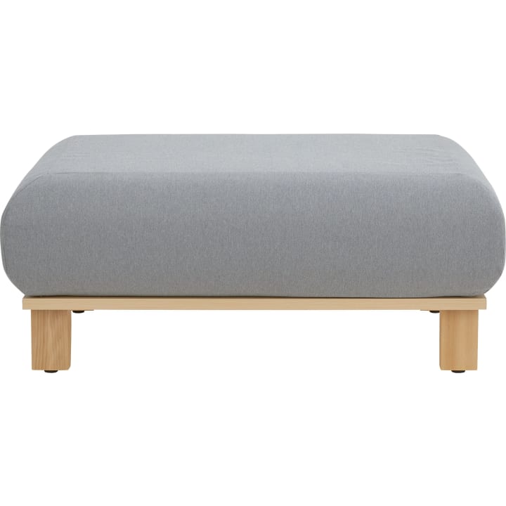 Ein rechteckiger Hocker mit einem hellgrauen gepolsterten Kissen und einem schlichten Sockel und Beinen aus hellem Holz, von vorne auf weißem Hintergrund.