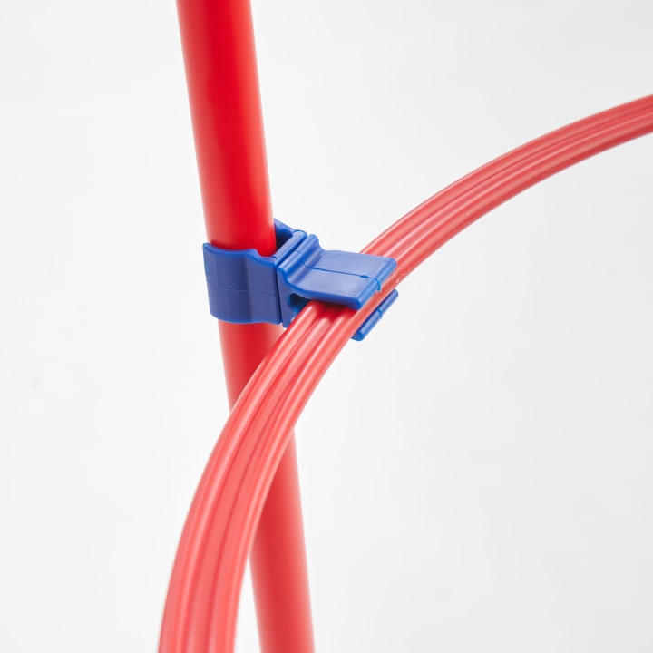 Nahaufnahme eines roten Plastikreifs, der mit einer blauen Plastikklammer an einer vertikalen roten Stange befestigt ist, vor einem schlichten weißen Hintergrund.