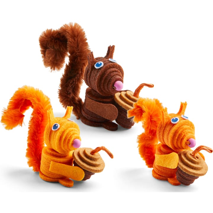 Drei handgefertigte Eichhörnchenfiguren aus Pfeifenreinigern und Filz, die jeweils eine Eichel aus Filz halten. Zwei sind orange mit gelben Details, und eines ist braun. Alle haben blaue und weiße Augen und flauschige Schwänze aus Pfeifenreinigern.