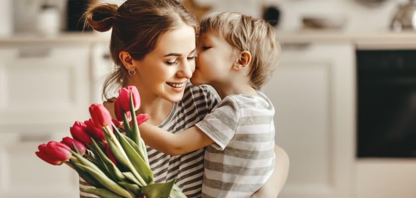 Muttertagsgeschenke basteln: Kind umarmt Mutter und schenkt Blumen