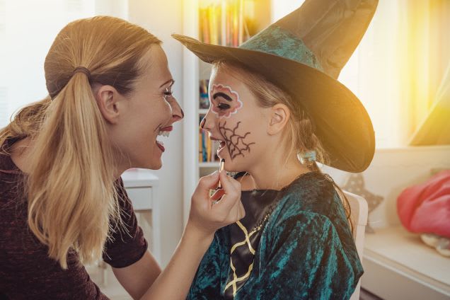 Kinder zu Halloween schminken: Mutter schminkt Tochter zur Hexe und malt ihr ein Spinnennetz auf die Wange