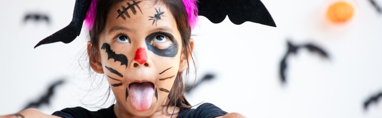 Kinder zu Halloween schminken: Mädchen ist als Fledermaus verkleidet und verzieht lustig das Gesicht 