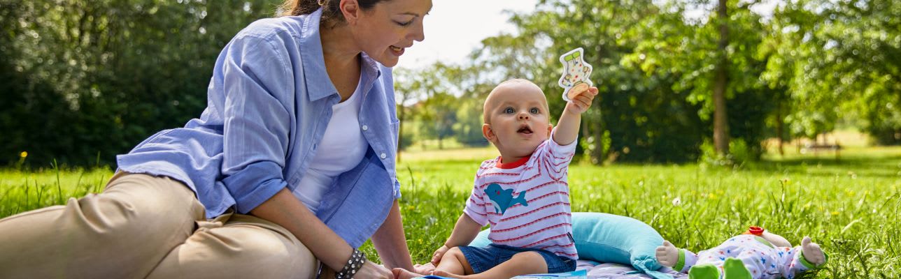 Erstausstattung Babys im Sommer: Kind sitzt mit Mutter auf Picknickdecke