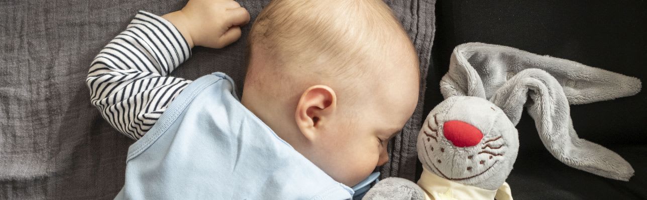 Erstausstattung Babys im Sommer: Kind liegt mit Schnullerhasen im Bettchen