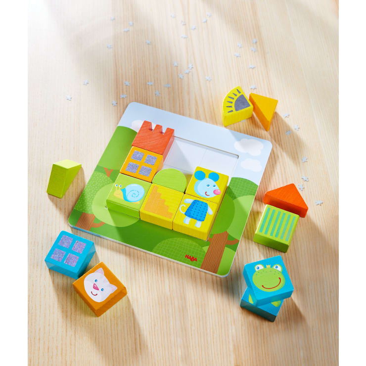 Ein farbenfrohes Holzpuzzle mit Blöcken mit Tiermotiven ist teilweise auf einer hellen Holzoberfläche zusammengesetzt. Einige lose geometrische Teile und kleine weiße sternförmige Konfetti sind um das Puzzle herum verstreut.