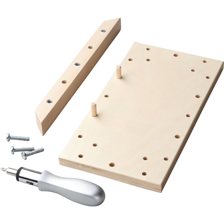 Eine Holzschablone mit mehreren Löchern, zwei Holzdübel, ein L-förmiges Holzstück mit Metalleinsätzen, drei Schrauben und ein Schraubendrehergriff mit Metallschaft, alles auf weißem Hintergrund.