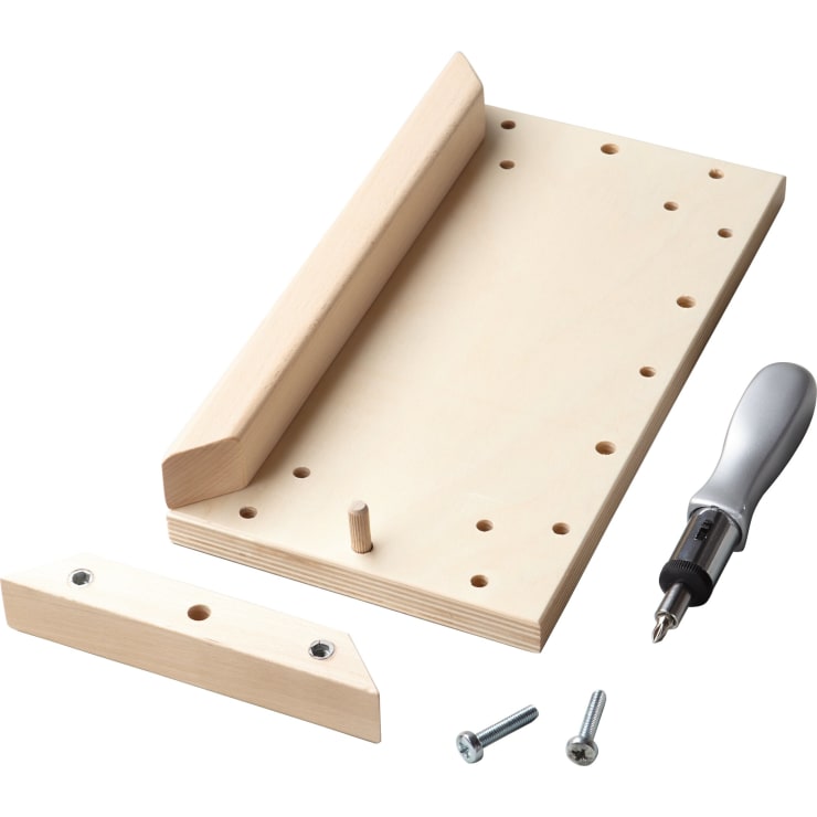 Eine Holzschablone mit einem abnehmbaren Teil, zwei Metallbolzen und einem Schraubendreher mit Bits, dargestellt auf weißem Hintergrund. Die Schablone hat mehrere Löcher und einen Holzpflock zum Ausrichten oder Montieren.