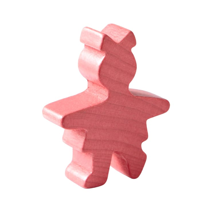 Eine rosafarbene Holzfigur in Form eines stilisierten Menschen, mit einfachen, abgerundeten Gesichtszügen und ohne Gesichtsdetails, die aufrecht vor einem weißen Hintergrund steht.