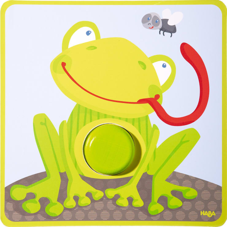Ein Cartoon-Frosch mit einer langen roten Zunge, der eine Fliege fängt. Der Frosch sitzt auf einer braunen Fläche, und auf seinem Bauch befindet sich ein runder grüner Knubbel, der darauf hindeutet, dass es sich um ein Puzzleteil handelt. Das Bild ist hellgrün umrandet.