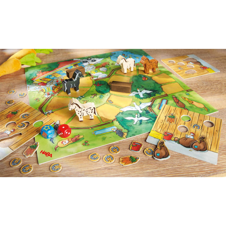 Das farbenfrohe Brettspiel für Kinder zeigt eine Bauernhofszene mit Tierfiguren, Würfeln, Karotten- und Hufeisenplättchen sowie Spielertafeln. Pferdefiguren aus Holz und Chips aus Pappe sind auf einem Holztisch verteilt.
