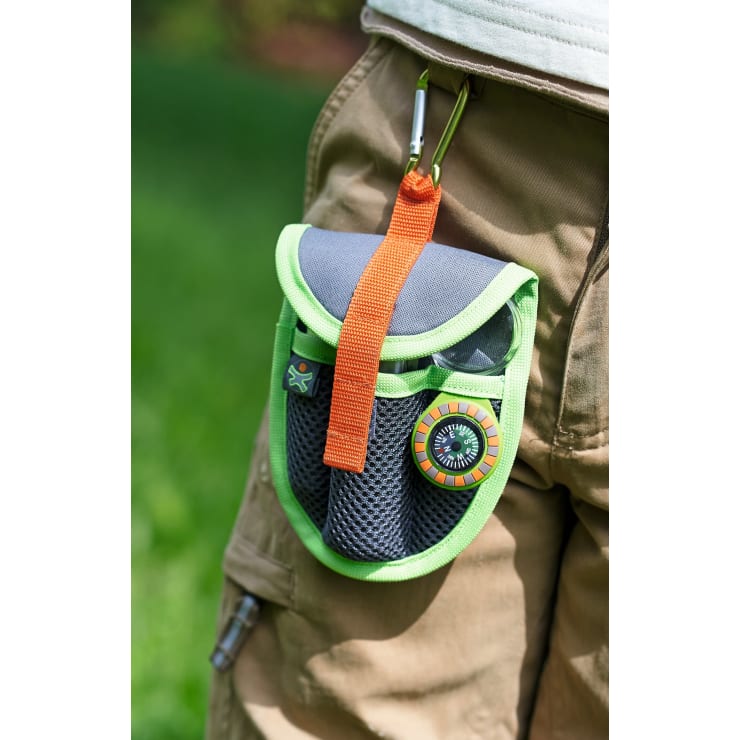 Eine kleine grau-grüne Tasche mit einem orangefarbenen Gurt und Karabiner ist an einer hellbraunen Hose befestigt. Die Tasche hat Netztaschen, einen Kompass, und ein grüner Hintergrund ist sichtbar.