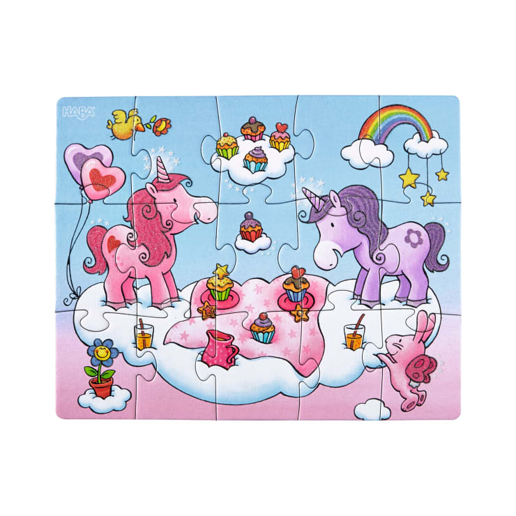 Ein fertiges Puzzle zeigt zwei Einhörner auf einer Wolke, umgeben von Cupcakes, Luftballons, Getränken und einem Schmetterling. Ein Regenbogen, Sterne und schwebende Wolken erscheinen am Himmel. Die Szene ist bunt und skurril.