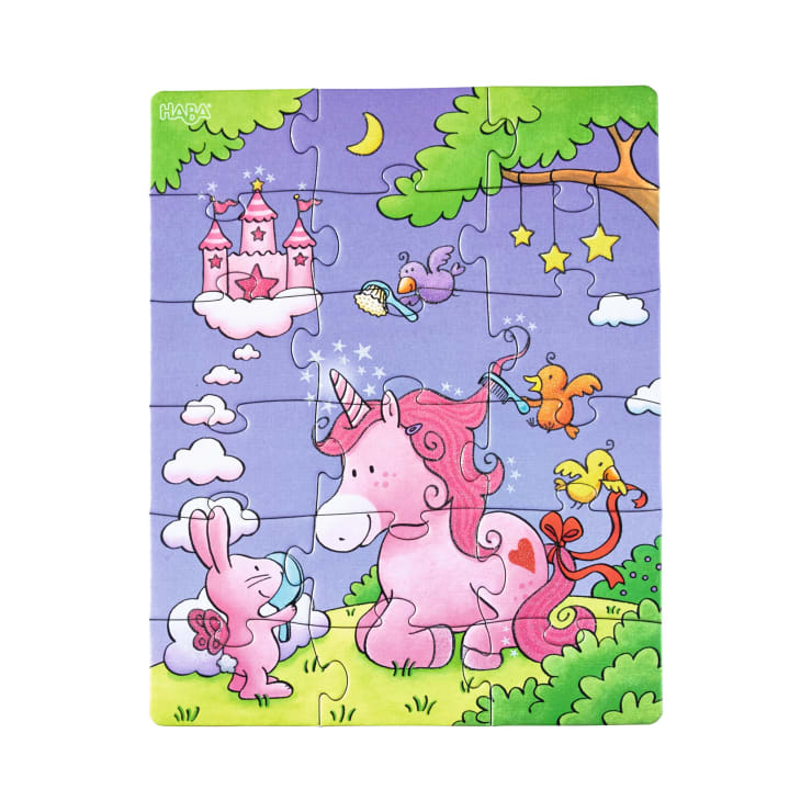 Ein fertiges Kinderpuzzle zeigt ein rosa Einhorn und einen rosa Hasen auf grünem Gras. Es gibt Vögel, Sterne, eine Mondsichel und ein rosa Schloss auf einer Wolke im lila Himmel, mit Bäumen auf der rechten Seite.