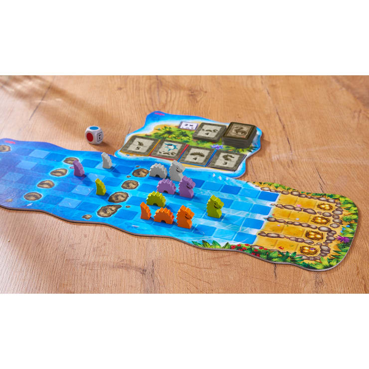 Auf einer hölzernen Oberfläche wird ein Brettspiel mit bunten, tierförmigen Spielsteinen auf einem blauen Pfad, einem Würfel mit farbigen Seiten und einem Spielfeld mit Zahlen und Symbolen aufgebaut.