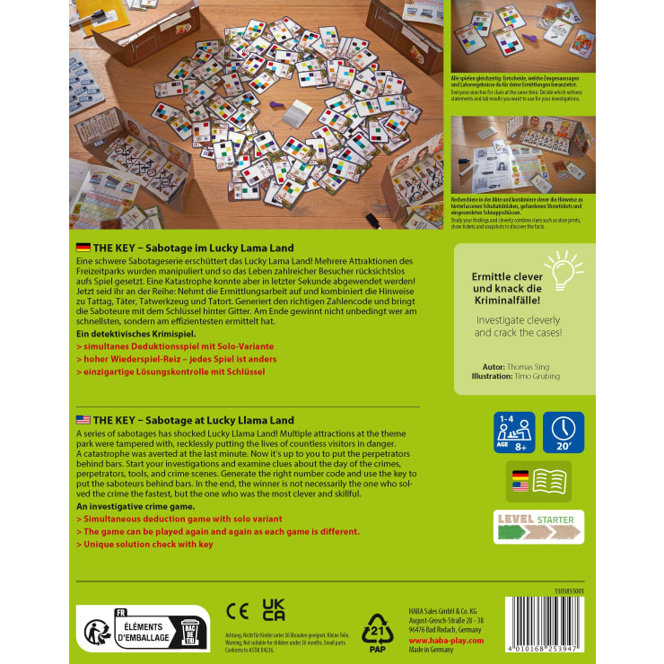 Ein Spielplan für THE KEY - Sabotage im Lucky Lama Land liegt auf einer grünen Fläche aus, umgeben von Karten, Hinweisplättchen und Spielfiguren. Die Spielschachtel und die Spielanleitung sind in der Nähe sichtbar.