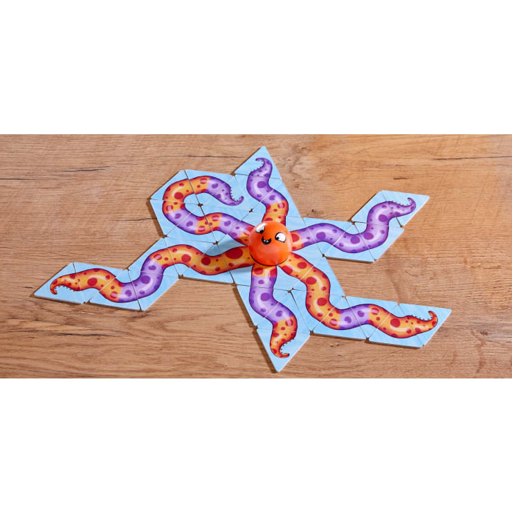 Ein Spielstein in Form eines orangefarbenen Krakenkopfes sitzt in der Mitte der passenden Puzzleteile, die die acht Tentakel des Kraken auf einer Holzoberfläche bilden.