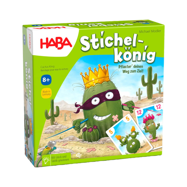 Eine grüne Brettspielschachtel mit dem Titel Stichelkönig zeigt einen illustrierten Kaktus, der eine Krone und eine Maske trägt und Spielkarten hält. Der Hintergrund zeigt eine Wüste mit Kakteen und blauem Himmel. Das Spiel ist für Kinder ab 8 Jahren geeignet.