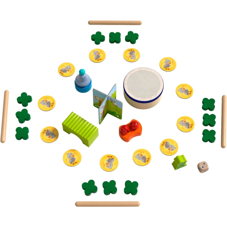 Eine Vielzahl von Kinderspielzeug und Spielfiguren, darunter hölzerne Kleeblätter, Tierplättchen, eine Trommel, ein Buch, eine Glocke, eine rote Rassel, ein Xylophon, Würfel und Holzstäbchen, die in einem symmetrischen Muster angeordnet sind.