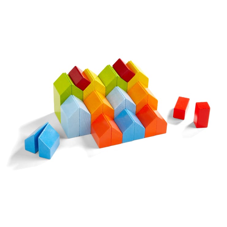 Mehrere bunte Holzklötze in verschiedenen Formen sind in einem ordentlichen, geometrischen Muster angeordnet, das an Reihen von kleinen Häusern erinnert. Zwei rote Blöcke und zwei blaue keilförmige Blöcke sind von der Hauptgruppe getrennt.
