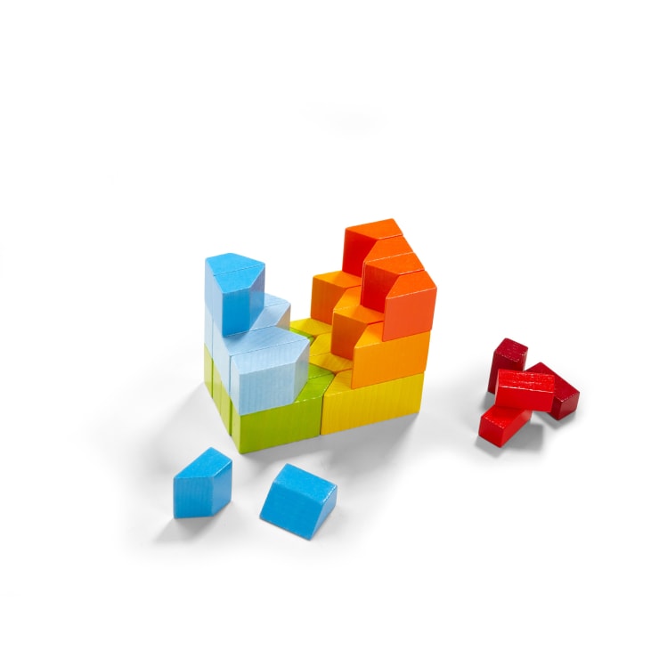 Bunte, ineinander greifende Holzklötze sind in einem Stufenmuster auf einer weißen Fläche angeordnet, mit blauen, roten, gelben, orangen und grünen Teilen. Mehrere rote und blaue Blöcke sind von der Hauptstruktur getrennt.