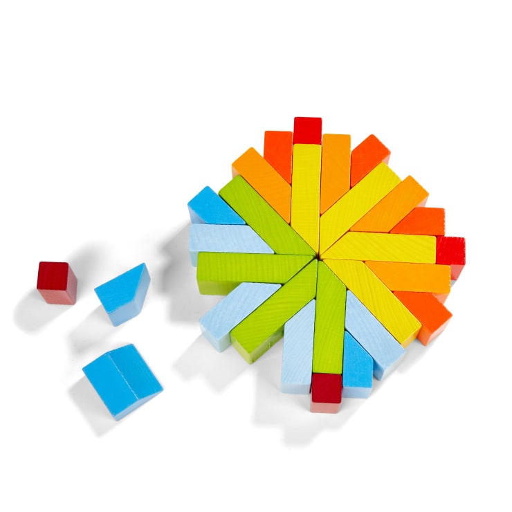 Eine kreisförmige Anordnung von bunten Holzklötzen, darunter rote, orange, gelbe, grüne und blaue Teile, mit vier von der Hauptgruppe getrennten Klötzen auf einem weißen Hintergrund.
