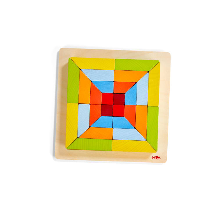 Ein Holzpuzzle mit bunten geometrischen Teilen, die in einem symmetrischen Muster auf einer quadratischen Grundfläche angeordnet sind. Die Teile sind rot, blau, grün, gelb und orange. Der Markenname HABA erscheint in der unteren rechten Ecke.